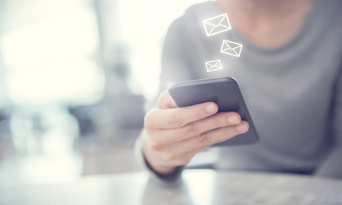 Eine Person die auf ein Handy schaut aus dem E-Mail Icons hervorkommen.